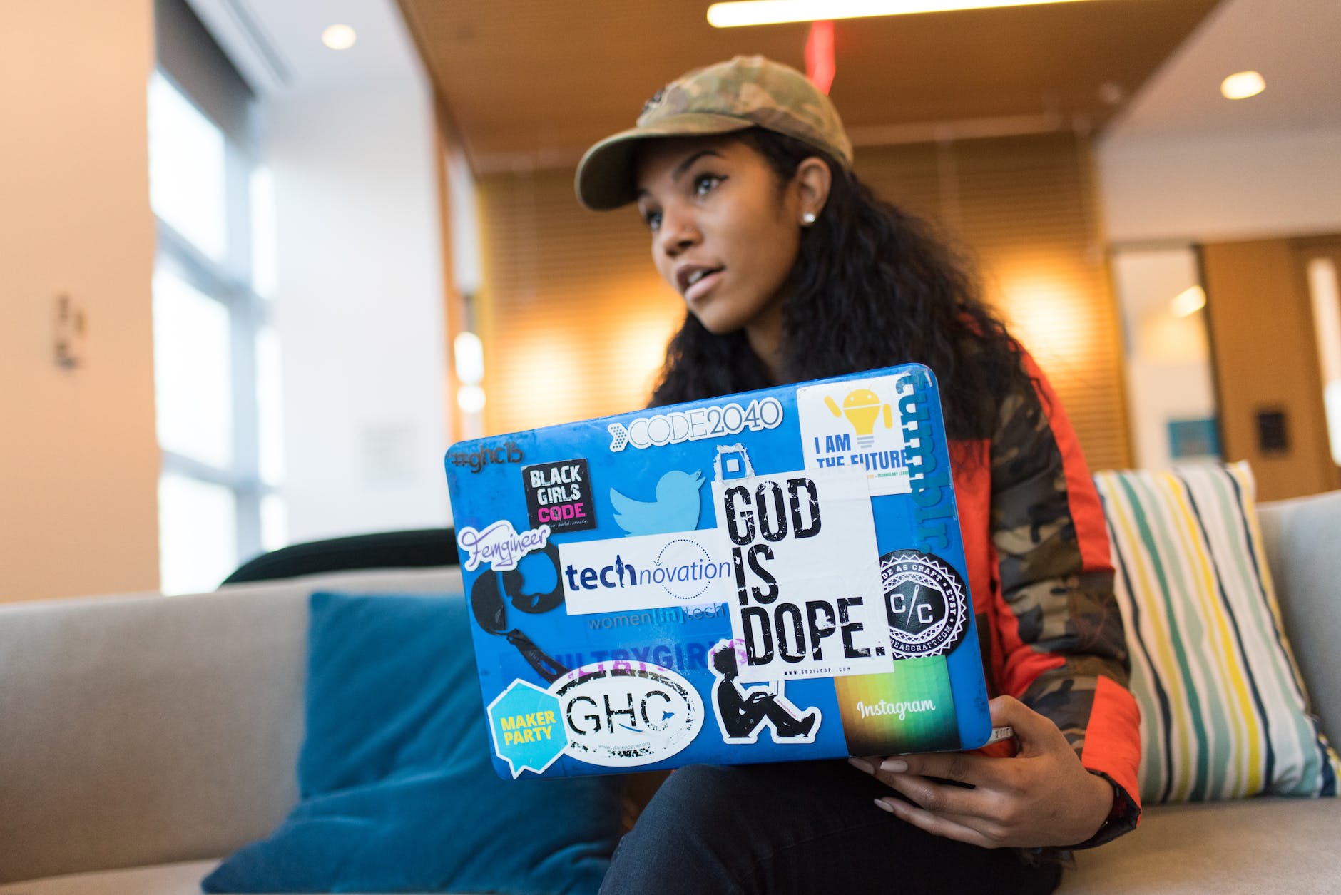 woman holds blue laptop computer while sits on sofa inside the room